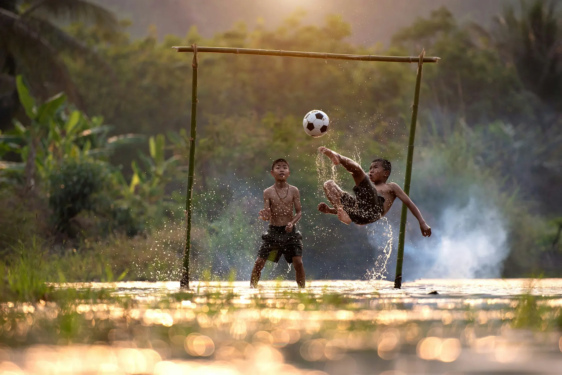 Dois jovens jogando futebol em um campo improvisado na água.